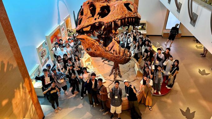 Students pose next to a dinosaur at a museum