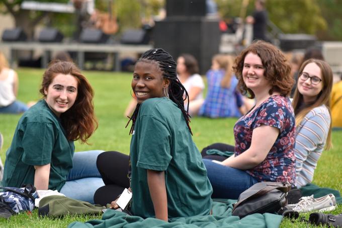 Four students sitting in the grass smiling at the camera