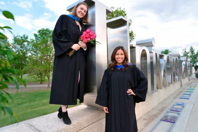Two women standing by the U of R sign