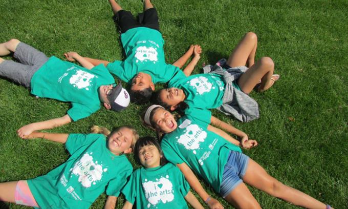 Children laying on the grass in a group wearing bright green tshirts at camp.