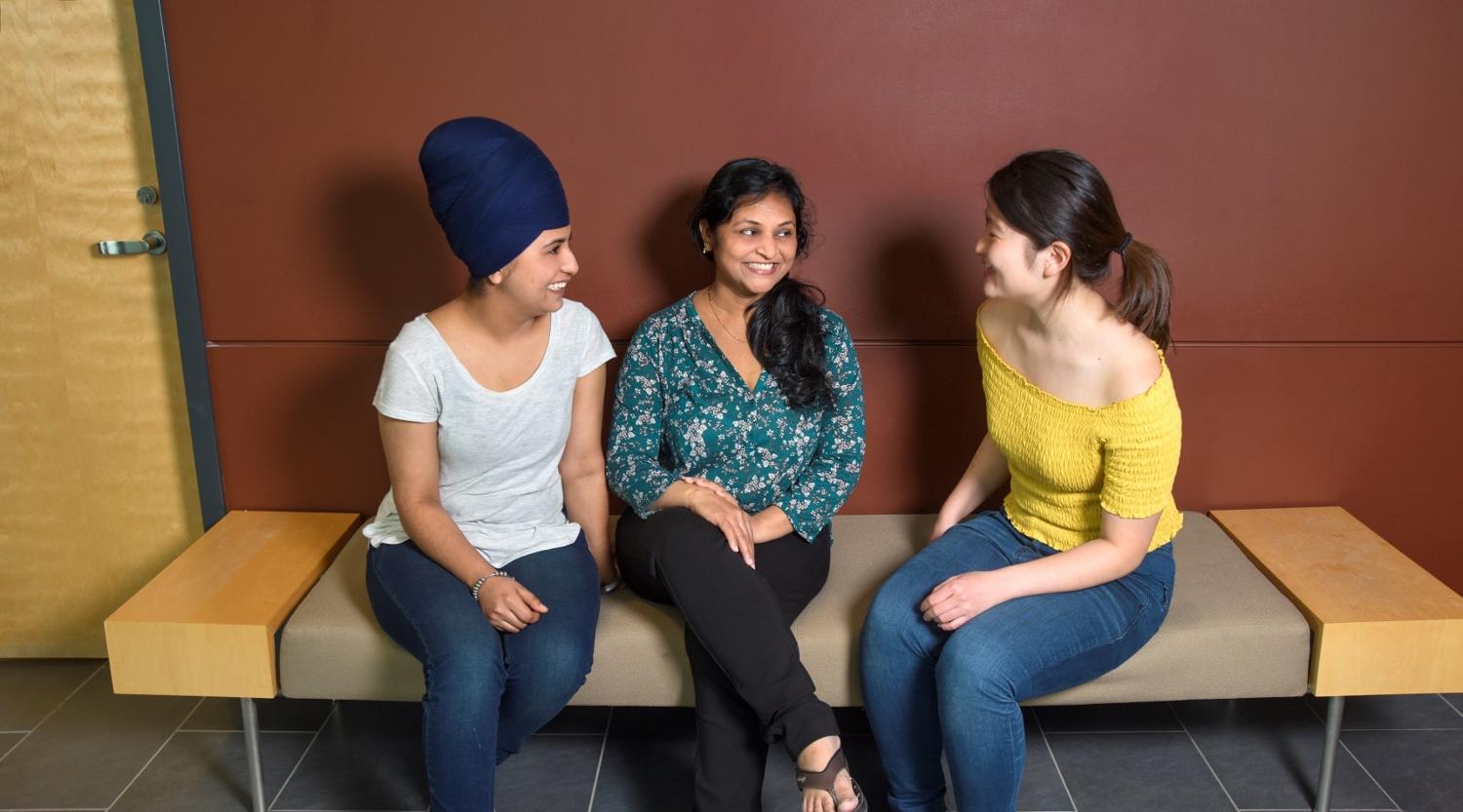 Three students sit and talk on a bench