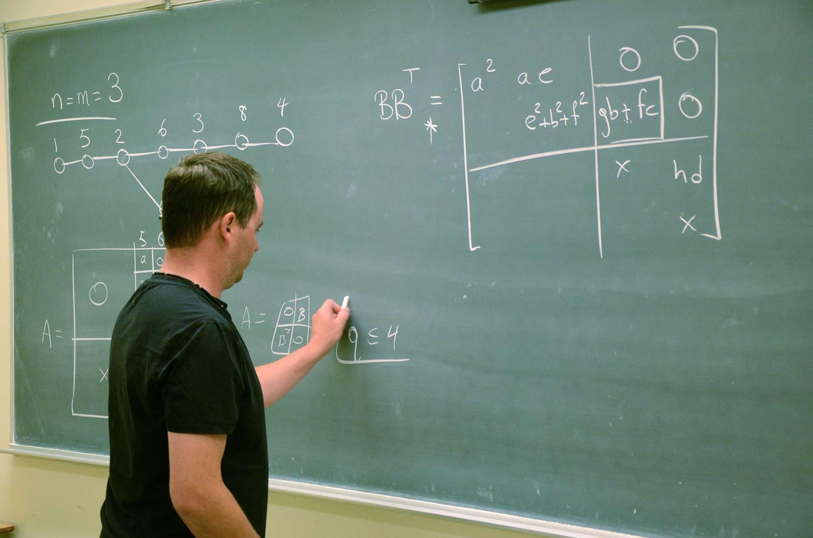 Professor writing math equations on chalkboard.