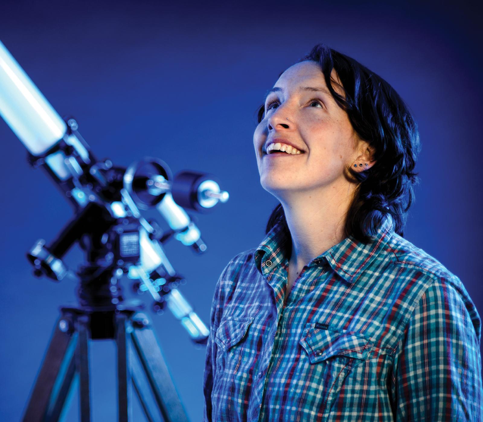 Professor looking up with a telescope behind her.