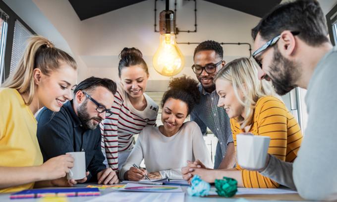 a group of people at work gathered around a colleague who is drawing an idea on a piece of paper