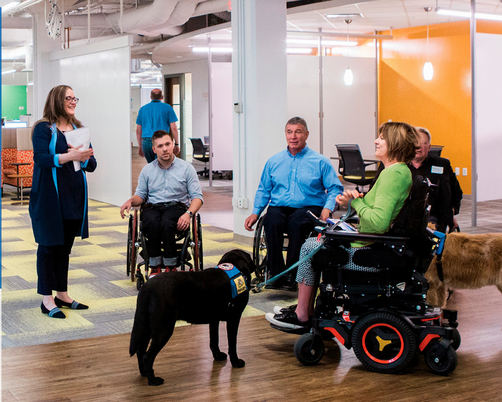 A group of people in wheelchairs and with guide dogs have a chat in a large lobby