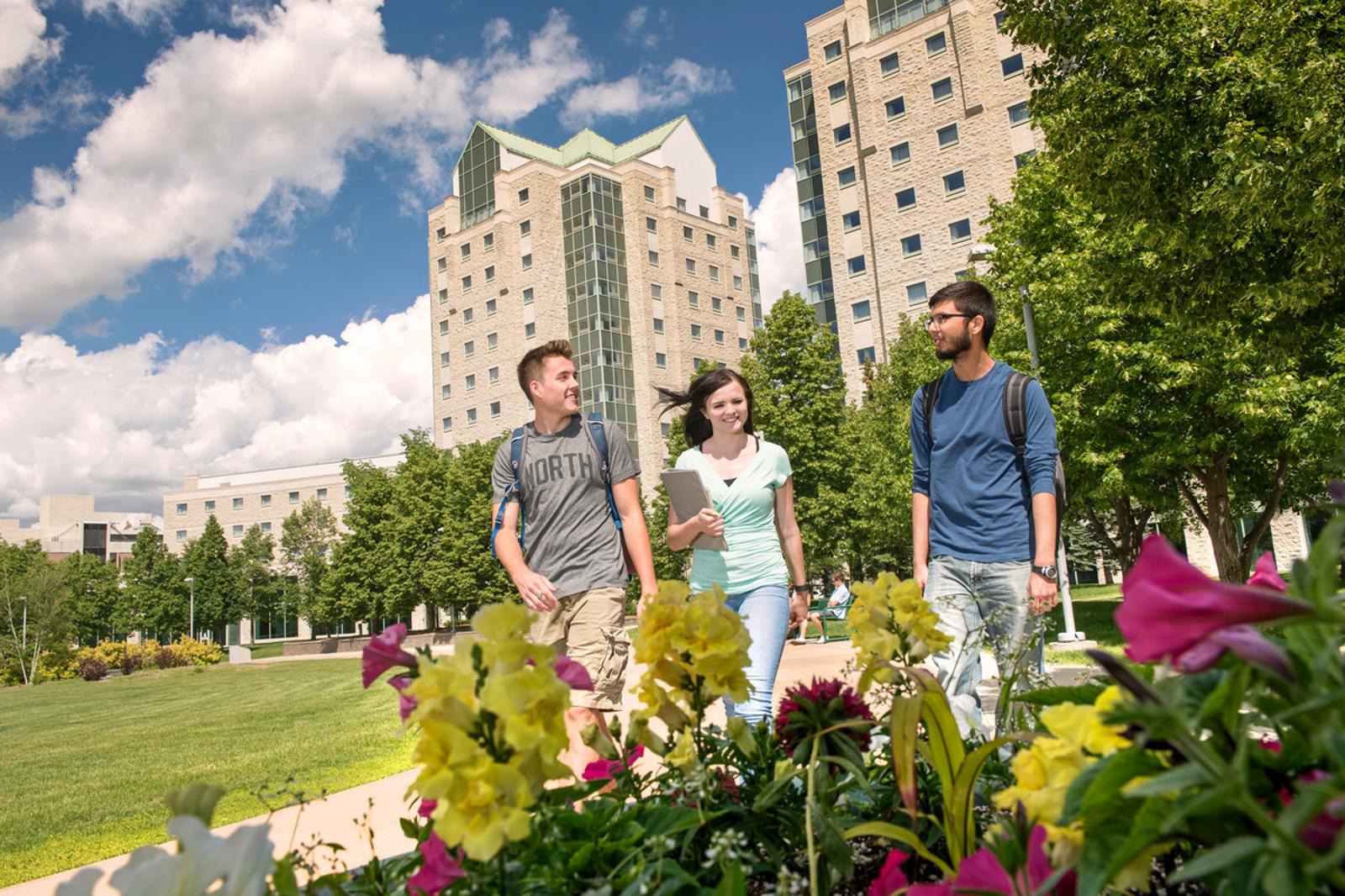 three students walking on campus with residence buildings in background