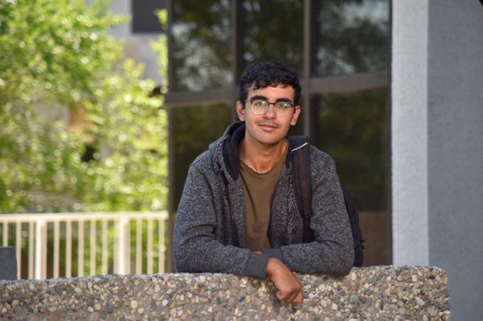 Male student leaning on stone wall