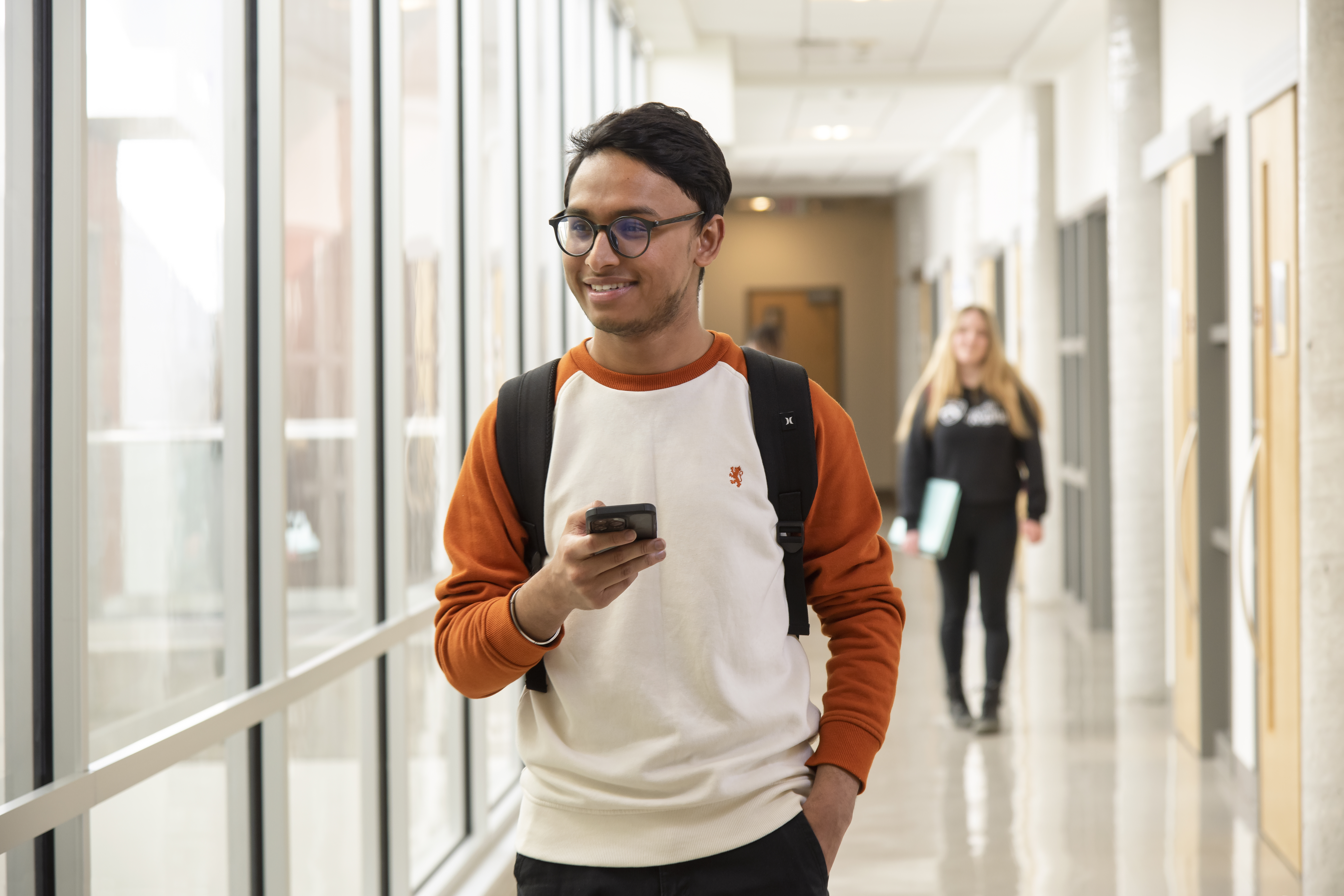 Student walking down hallway smiling with phone in hand. 