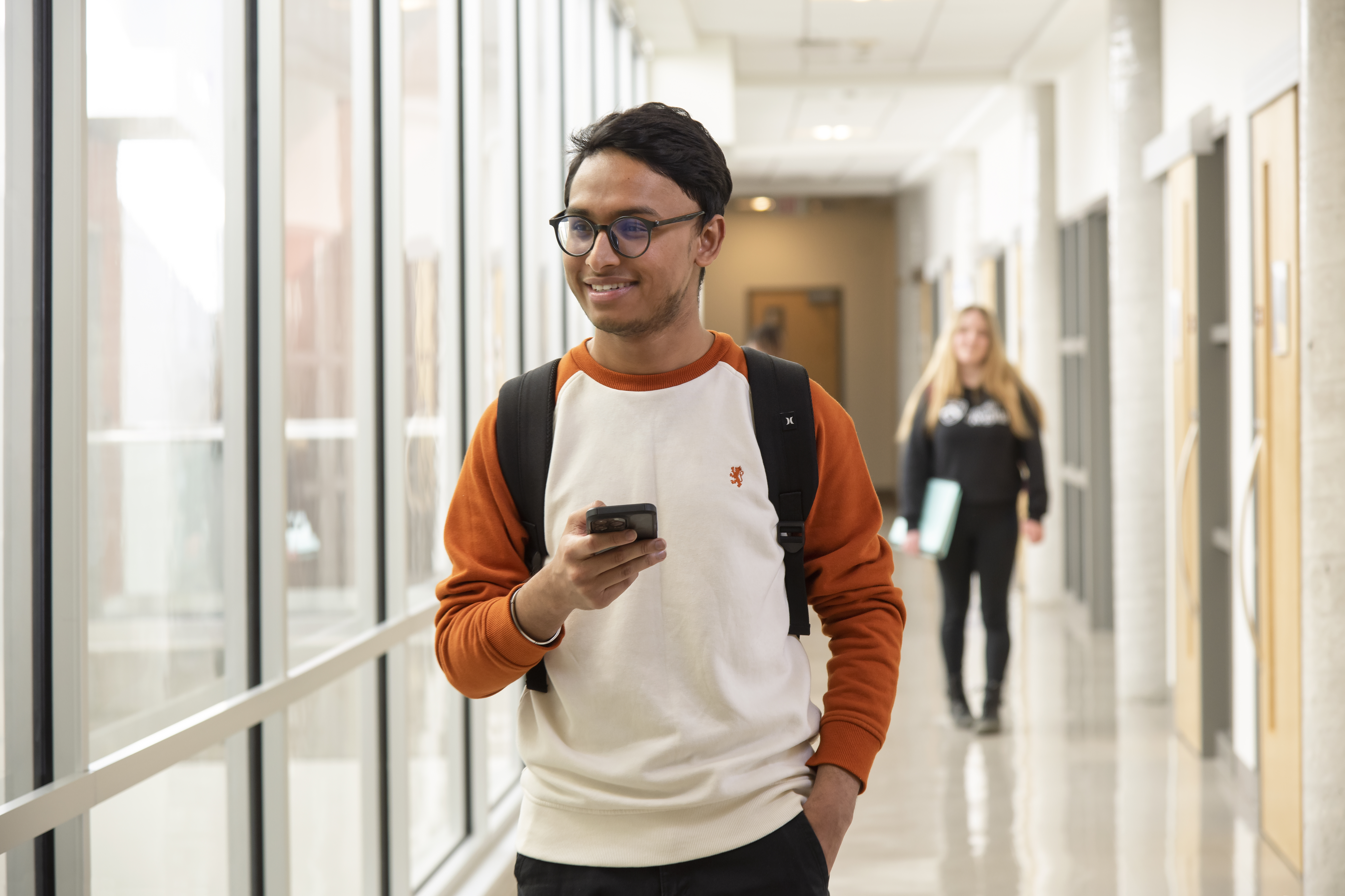 Student walking down hallway smiling with phone in hand.