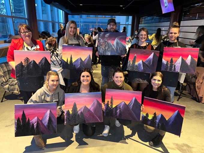 group holding up paintings of mountains at sunset