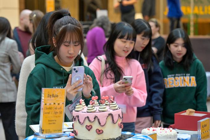 Students standing, bidding on cakes and taking pictures with cellphones