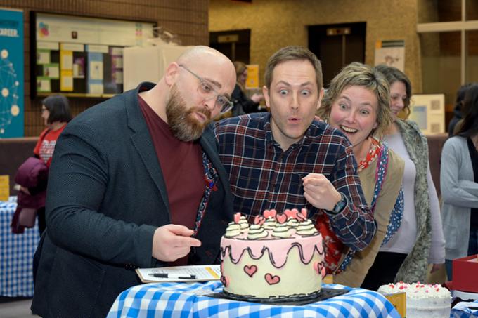 Three people look excitedly at a cake