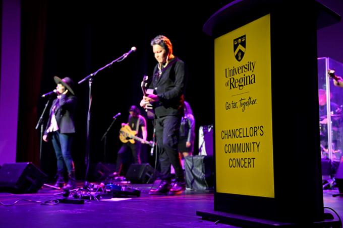 Musicians Digging Roots playing on stage next to U of R podium with sign Chancellor's Community Concert.