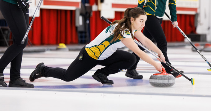 Female curler sliding on ice, releasing a curling stone.