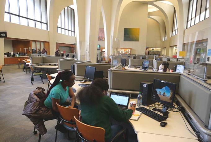 Students sit at a computer desk in the library