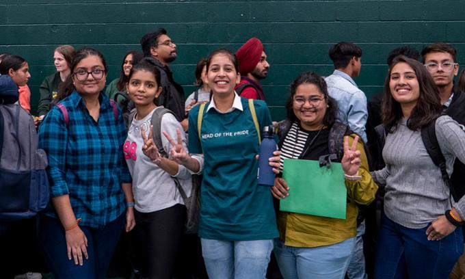 Group of diverse students with backpacks stand smiling at the camera on campus.