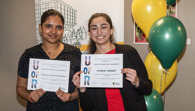 Two smiling individuals standing next to yellow and green balloons.
