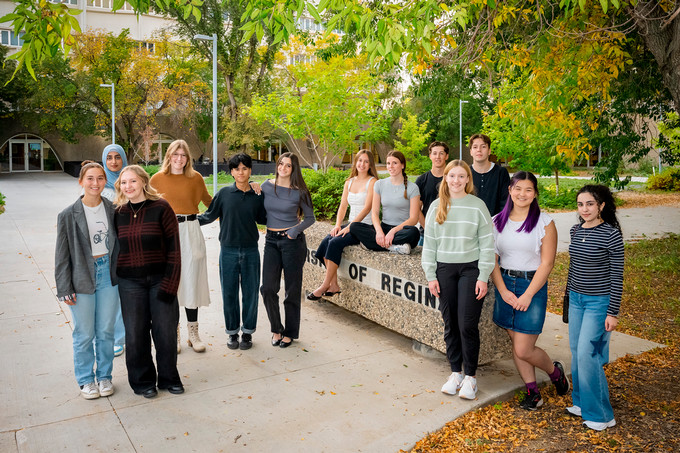13 students stand outside on fall day.