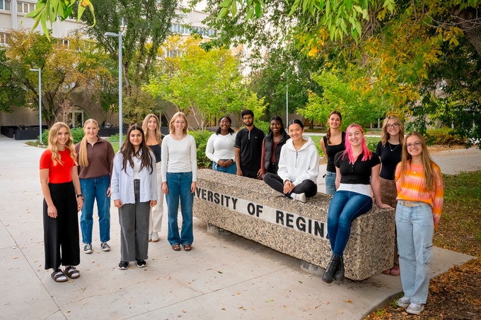 13 students stand outside on fall day.