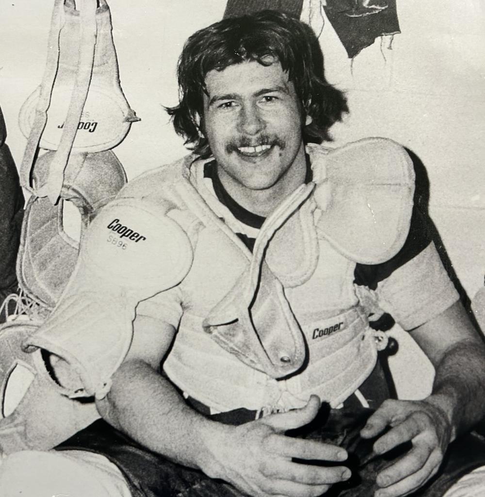 Man sits on bench wearing hockey gear.