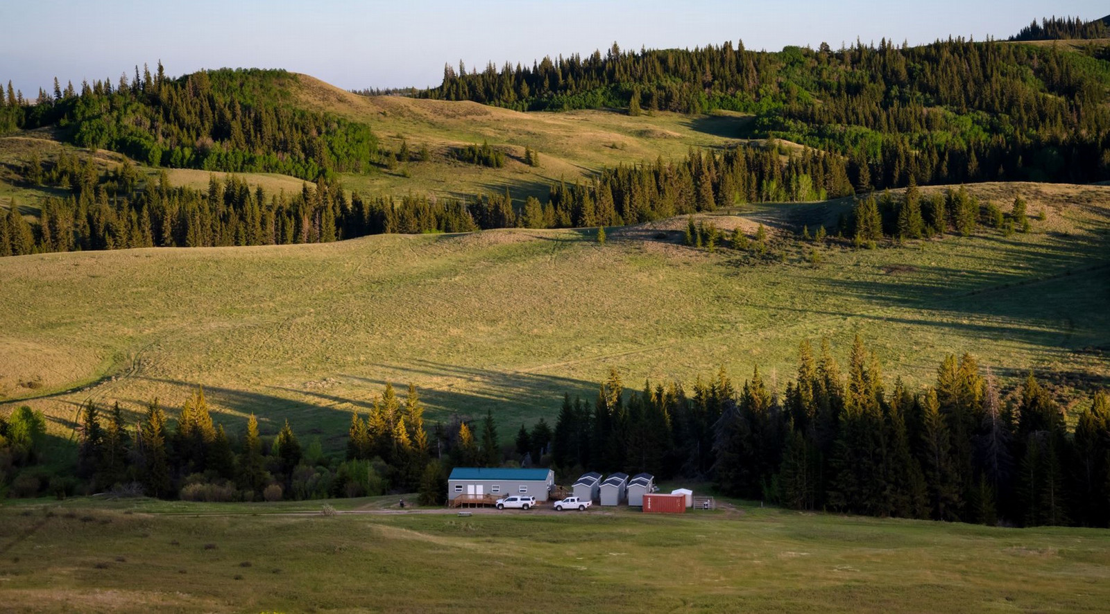 A single-story building and six small bunk rooms at the base of rolling hills.