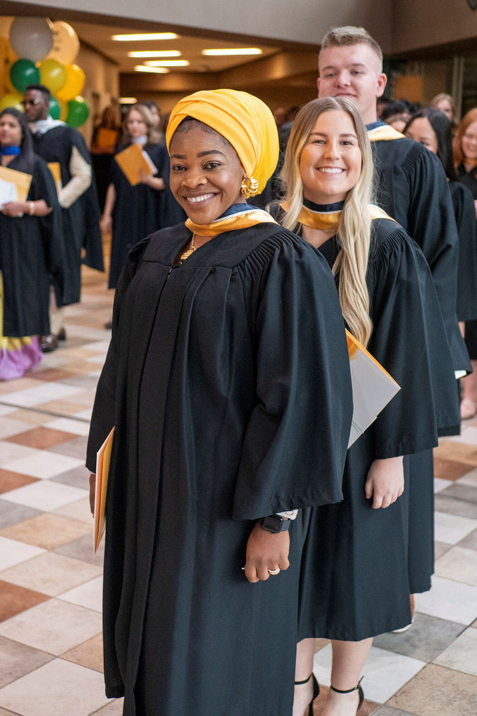 Three smiling students lined up in full convocation gowns.