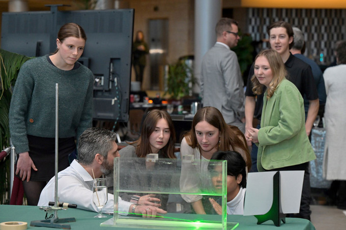 People observe a rectangular glass container filled half way with water and a green light projected onto it.