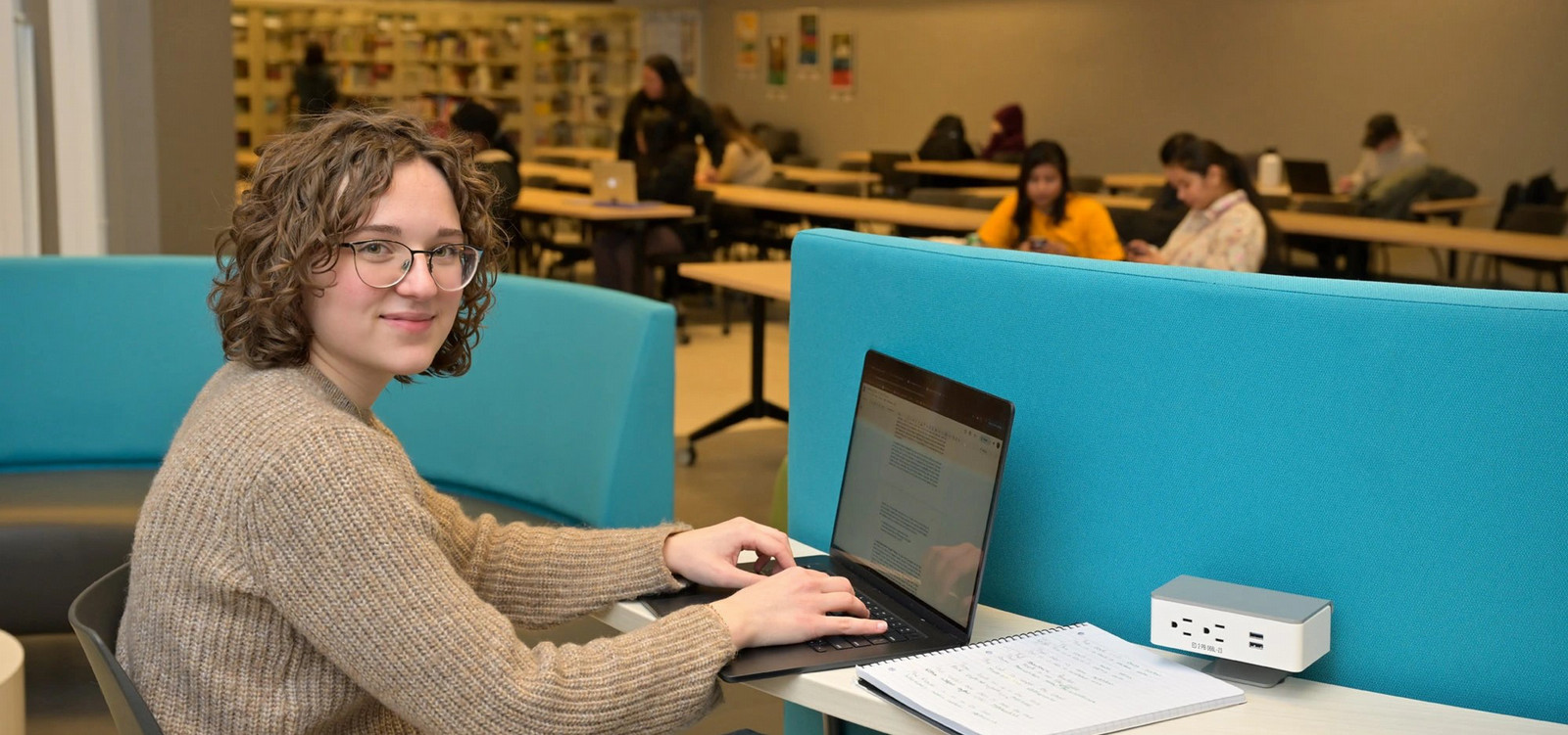 Student smiles sitting at desk with laptop.