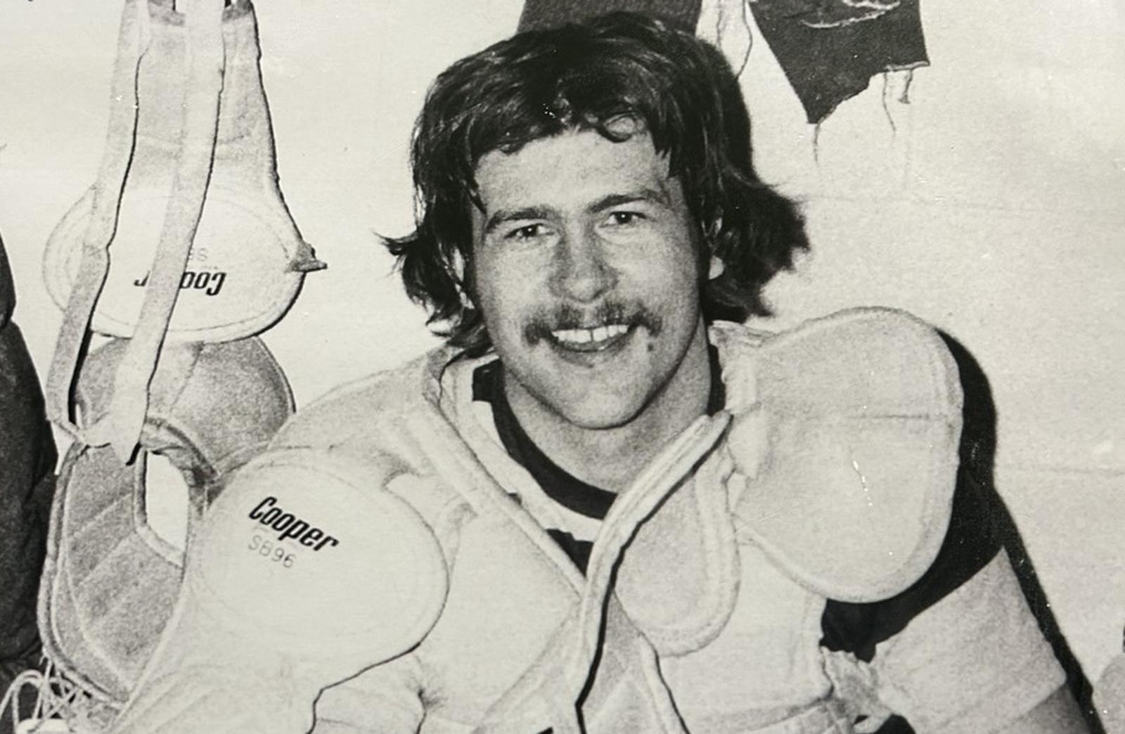 Man sits on bench wearing hockey gear.