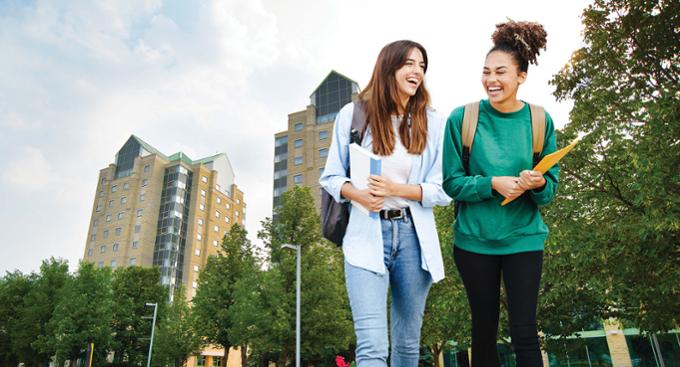 Two students walking together on U of R Campus in the Academic Green, with the U of R residence towers in the background.