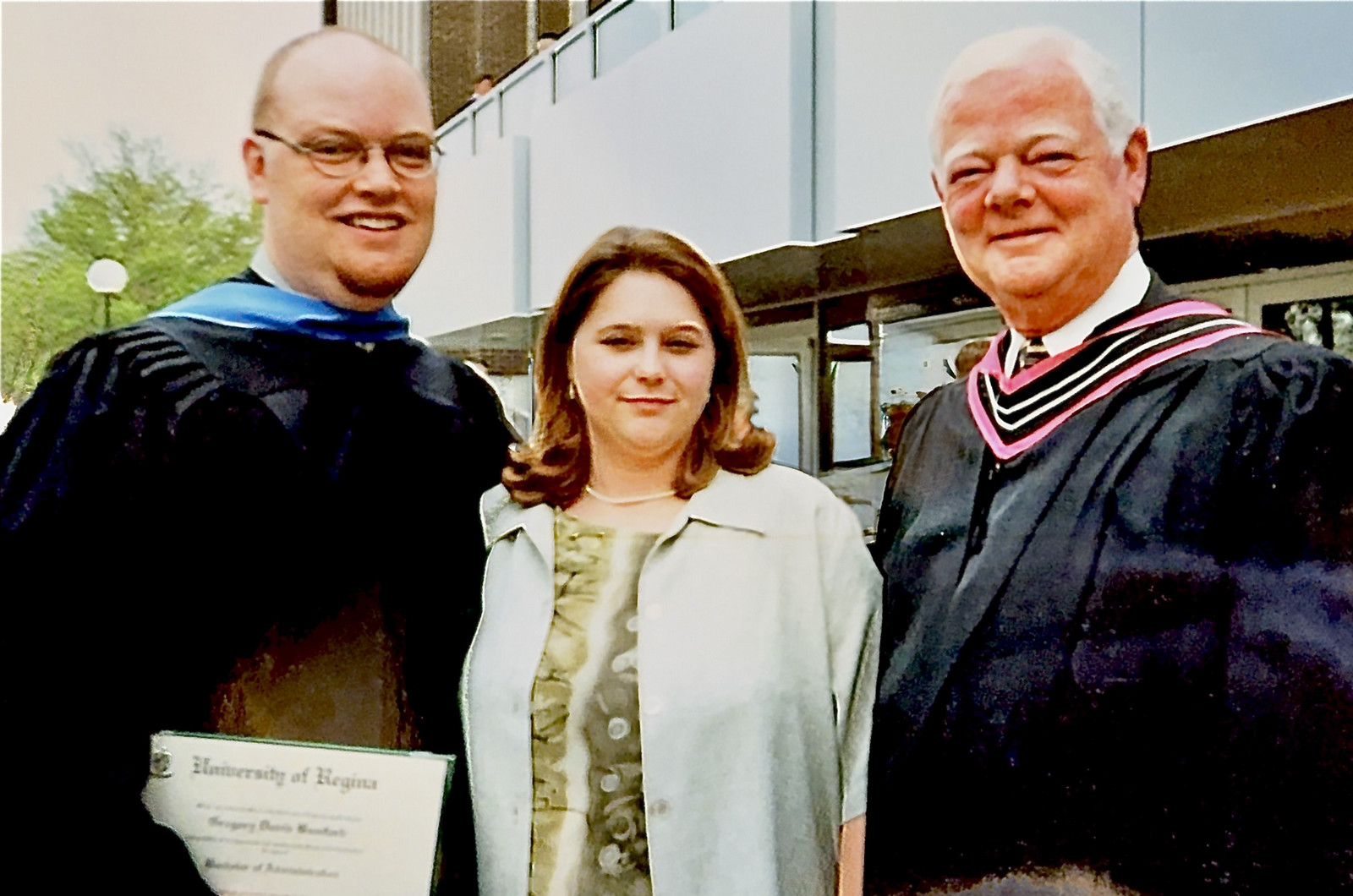 Three smiling individuals standing outdoors.