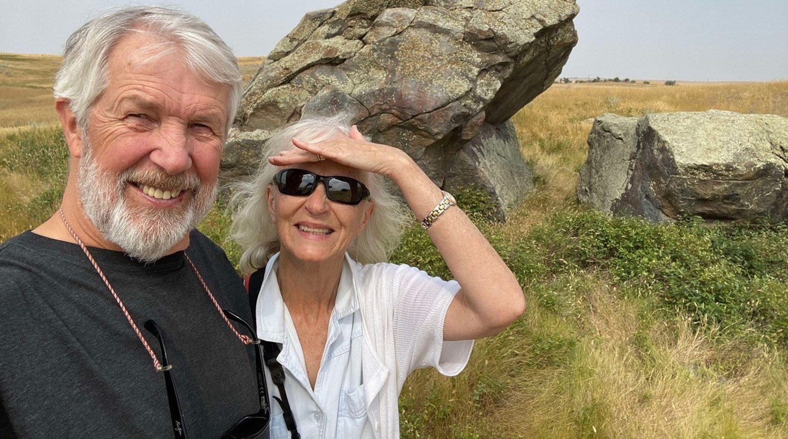 Two people smiling stand side by side with mountains in background