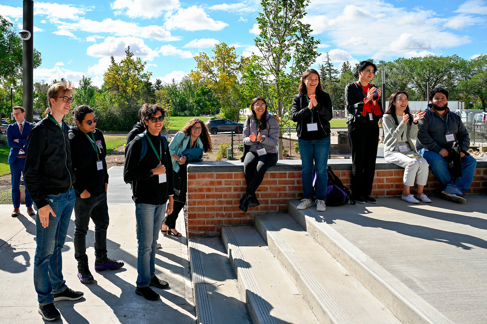 A large group of people sitting and standing outdoors on a sunny day.