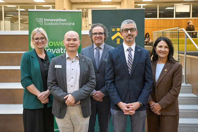 Five smiling people stand looking at the camera with pull up banners behind them.
