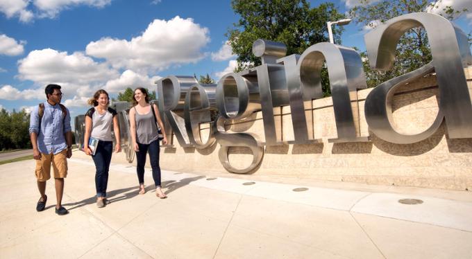 Three students walking by of U of R sign