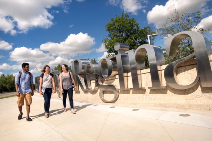 Three students walking outside by U of R sign