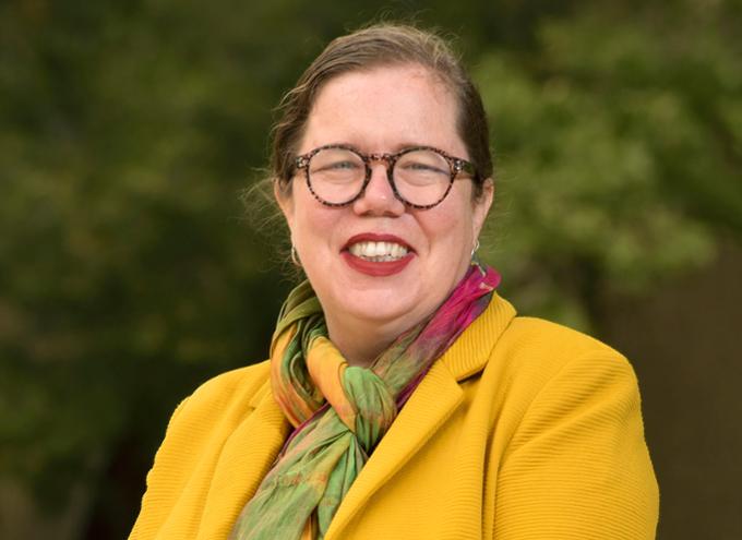 Dean Dea smiles outside wearing a yellow blazer