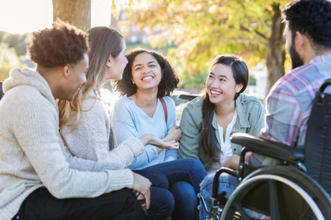 A small group of students are outside, laughing and chatting on a sunny Fall day.