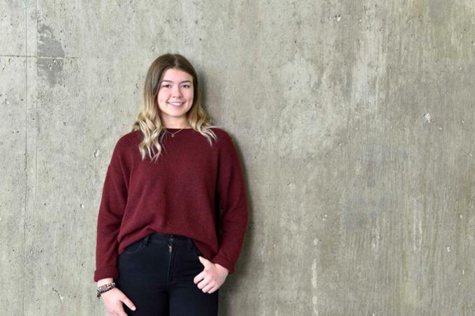 Female student in red sweater leaning agains a wall