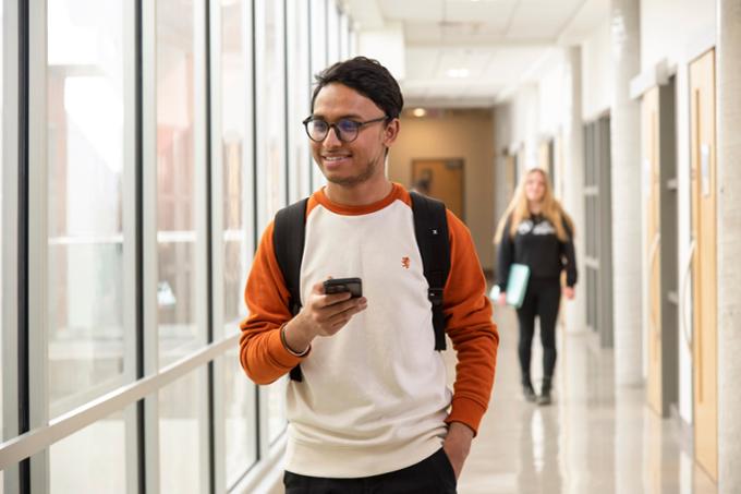 A student walking down a hallway phone in hand.