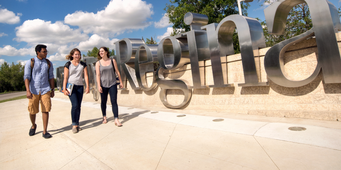 3 students walking in front of the UofR sign