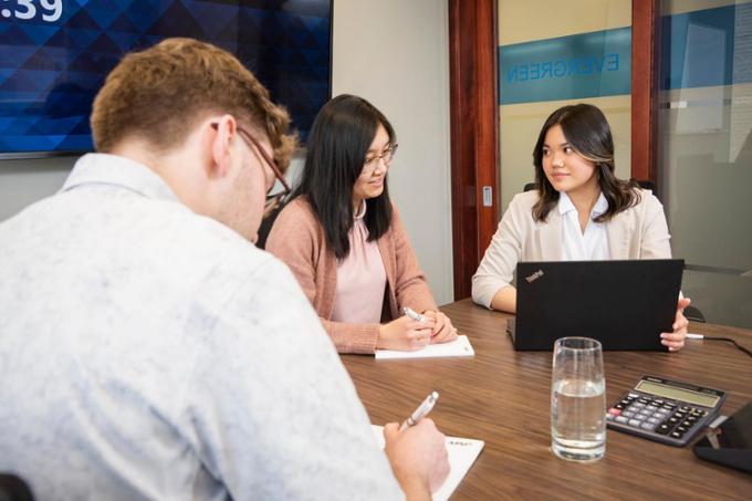 Three students use a computer together at a desk