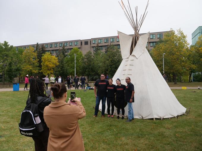Four students have their photo taken standing in front of tipi at tipi raising competition.