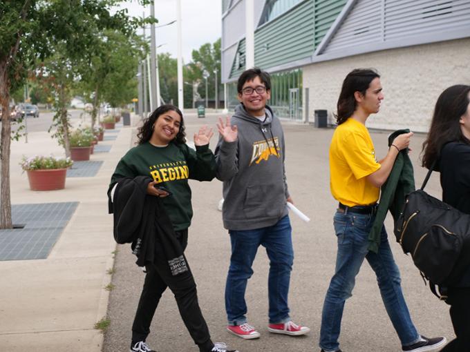 Three smiling students walking and one waving.