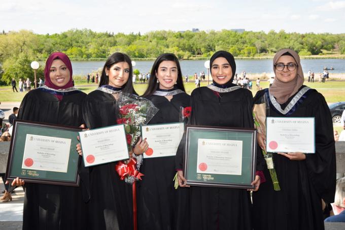 Five students posing and displaying their degrees