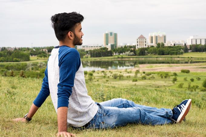 A student sitting on the grass in Wascana Park, looking out over Wascana Lake