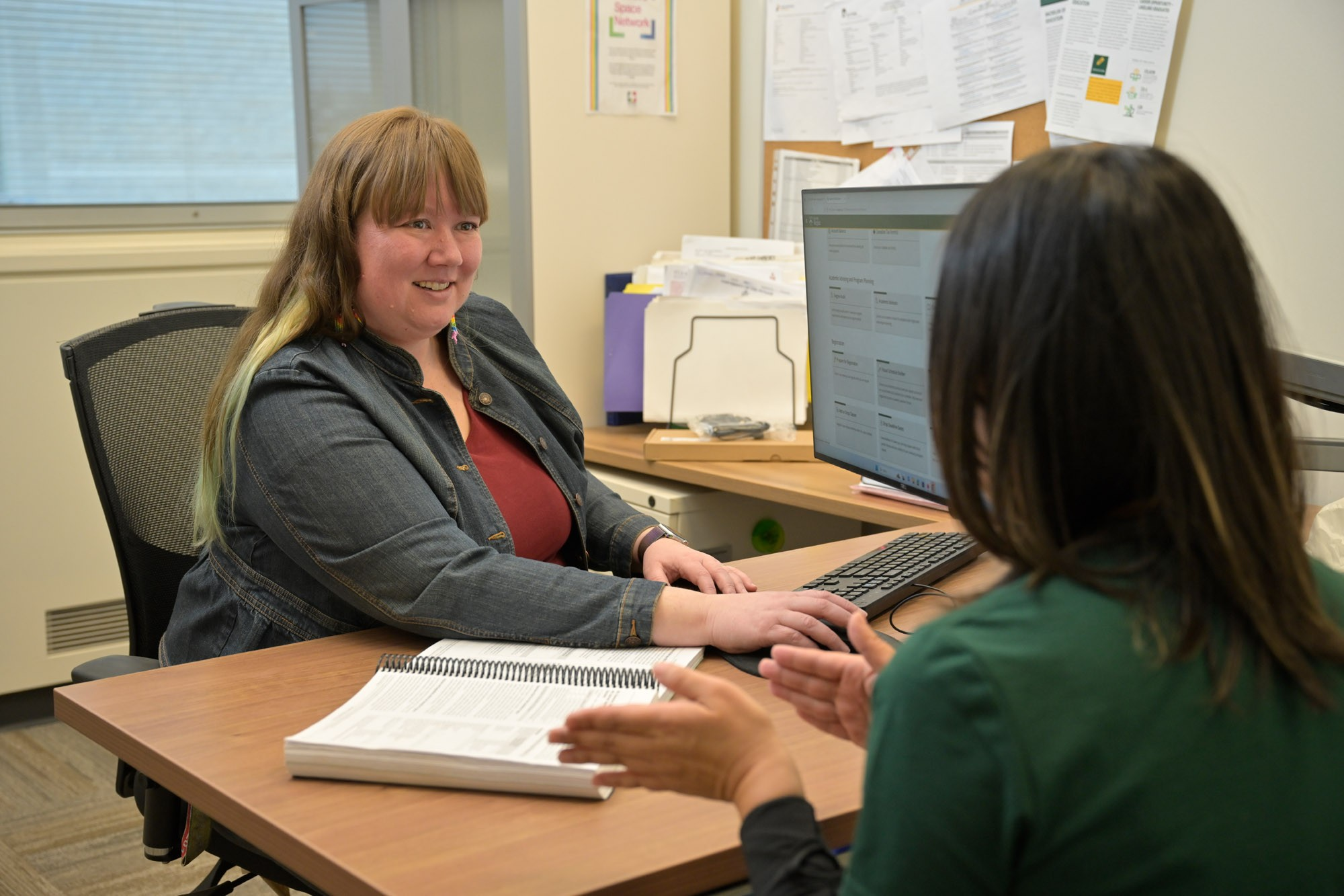 An advisor sitting at their desk speaking with a student