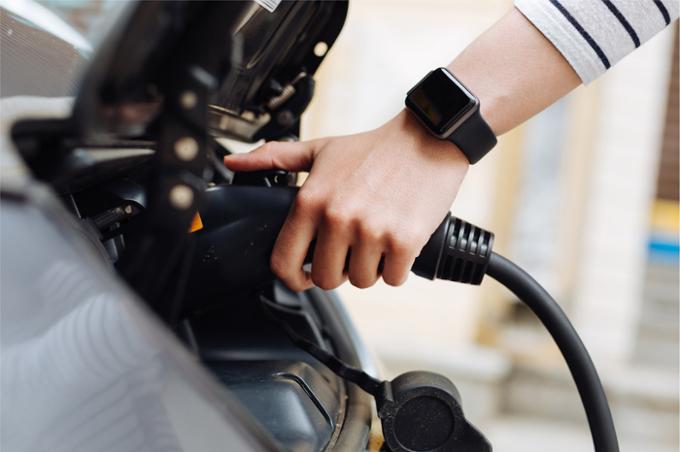 A hand charging up an electric car with an electric pump.