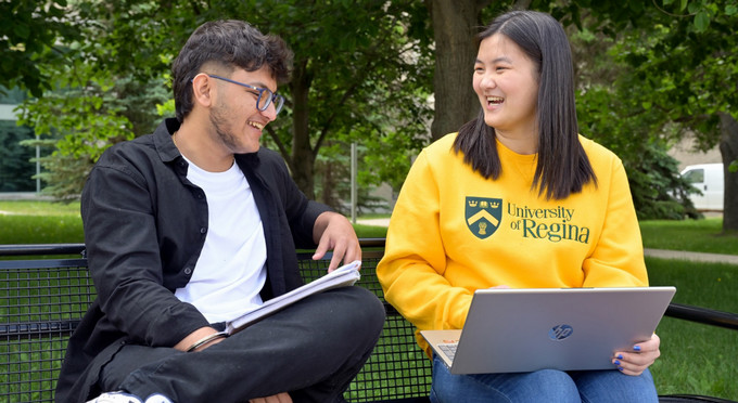 Two people sitting on a bench and looking at a computer
