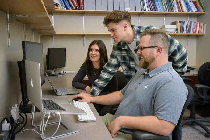 Three people looking at a computer in a office setting
